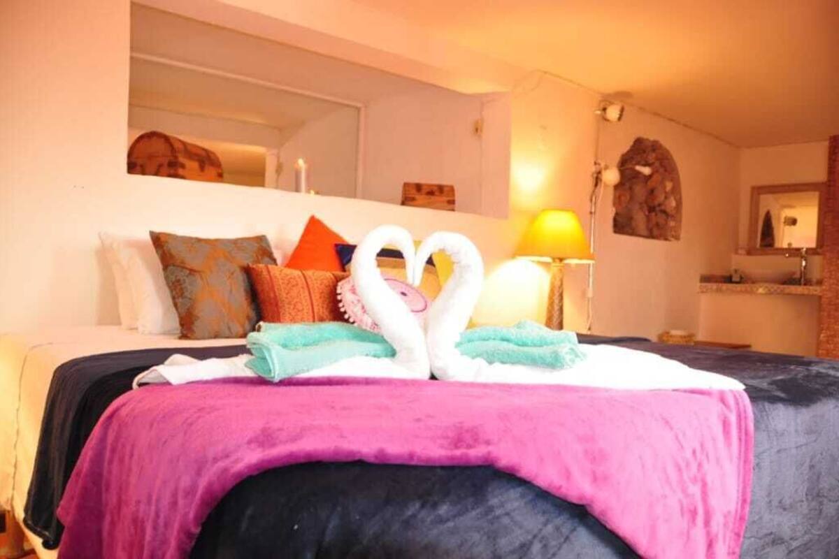 A hotel room with a bed, pillows, a lamp, and a mirror.