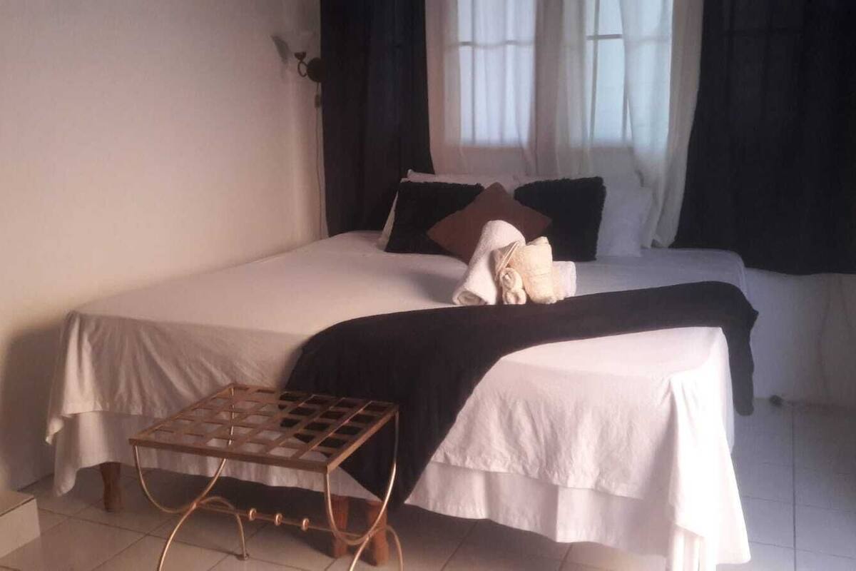 A bedroom with a bed, a small wooden side table, and a window with curtains.