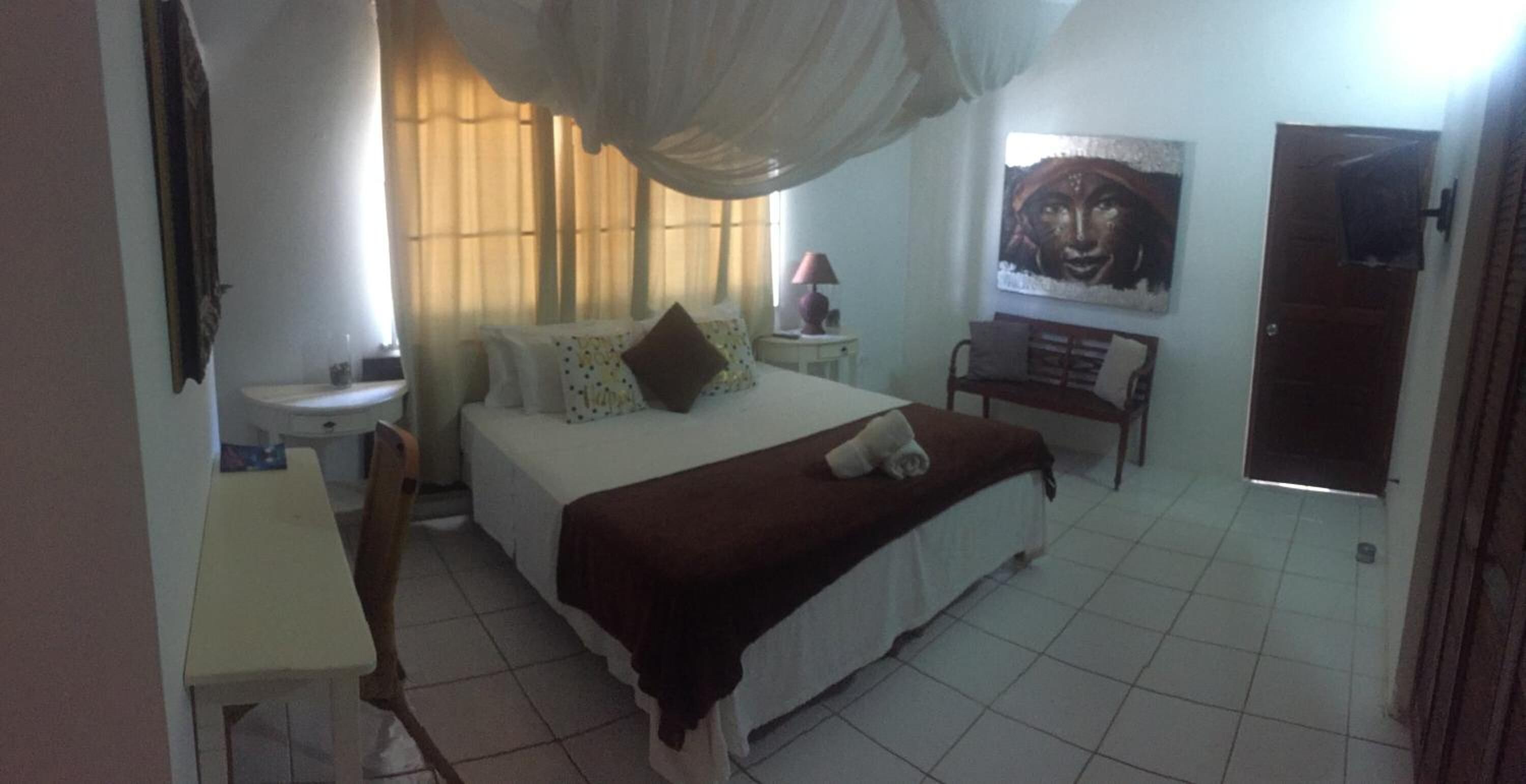 A bedroom with a bed, bedside table, lamp, and a painting on the wall.