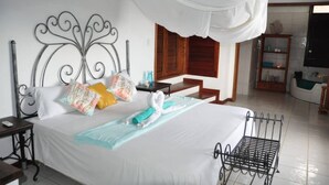 A hotel room with a bed, a nightstand, a bedside table, a window with wooden shutters, a bathroom with a bathtub, and a white canopy over the bed. - Oceanview B&B Curacao (Soto)