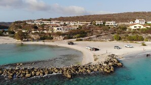 A coastal area with a sandy beach, rocky shoreline, and a row of buildings in the background. - Oceanview B&B Curacao (Soto)