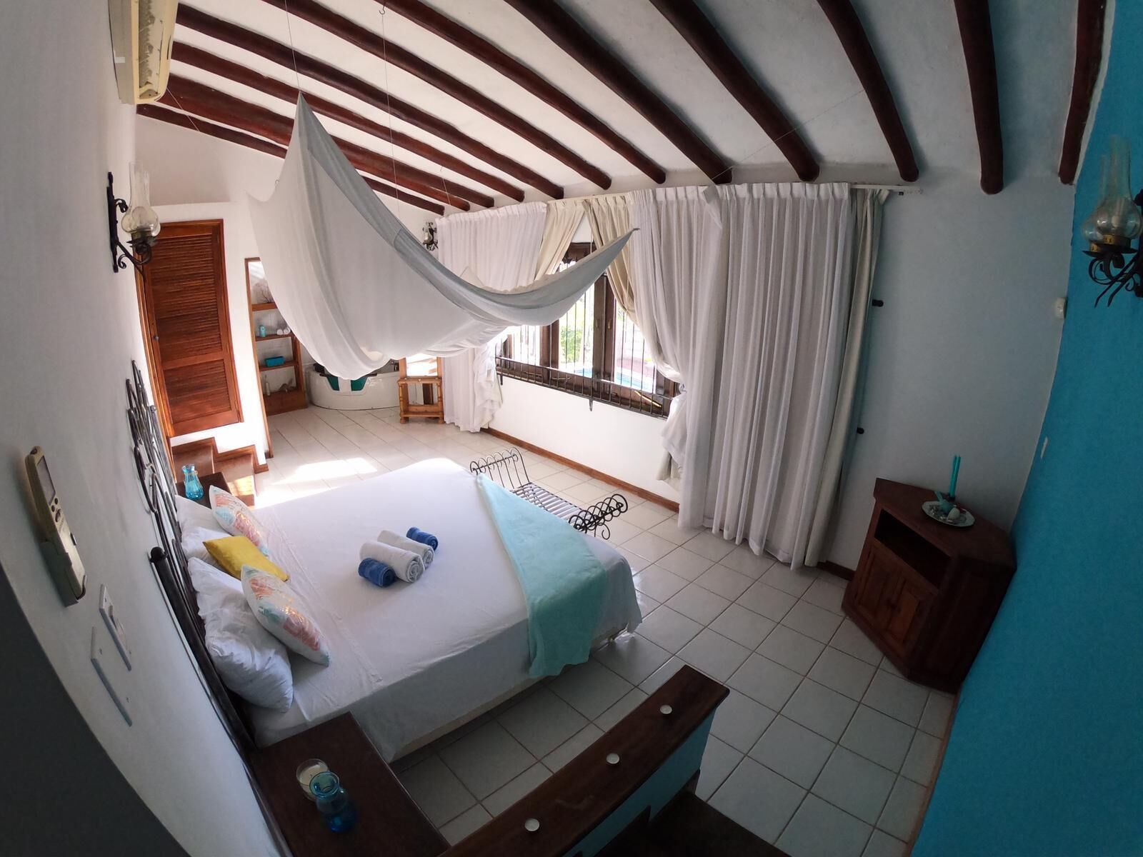 A bedroom with a bed, a window with curtains, a wooden bench, and a small table.