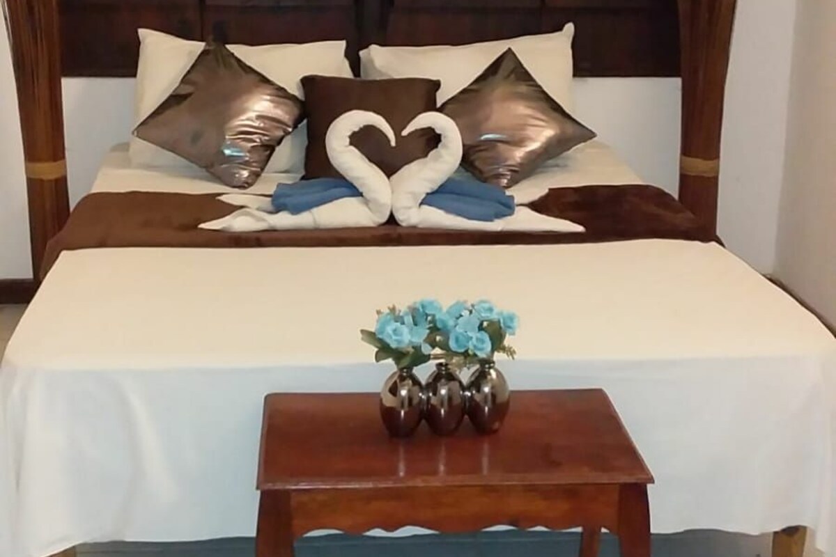 A bedroom with a large wooden headboard, a bed with white bedding, and a small wooden table with a vase of flowers.