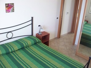 A bed with green striped bedding, a bedside table with a lamp, and a door leading to another room. - Le Terrazze sul Mare (Valledoria)