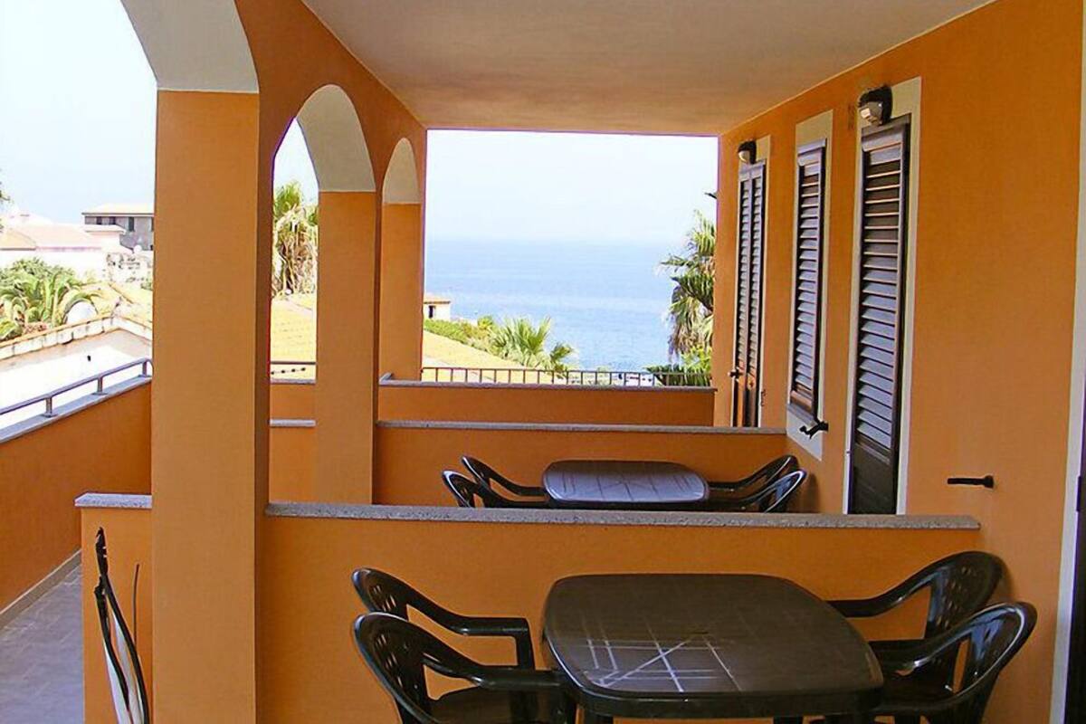 Un balcon avec une table et des chaises, une vue sur l’océan et un bâtiment aux murs orange.