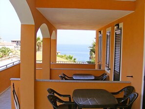A balcony with a table and chairs, a view of the ocean, and a building with orange walls. - Le Terrazze sul Mare (Valledoria)