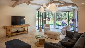 A spacious living room with a large TV, comfortable seating, and large windows offering a view of the outdoors. - Domaine du Buc  Les Gites de Prestige (Marssac-sur-Tarn)