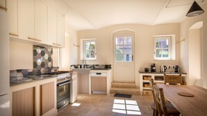 A modern kitchen with a central island, built-in oven, and a dishwasher. There are two windows providing natural light and a view of the outside. - Domaine du Buc  Les Gites de Prestige (Marssac-sur-Tarn)