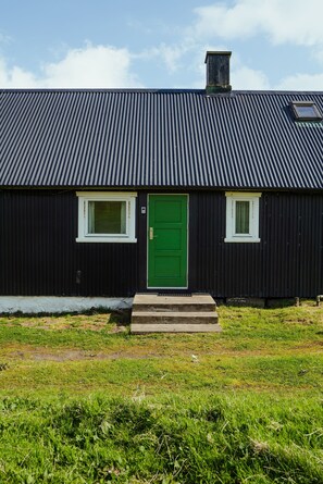 A black building with a green door, two windows, and a chimney. - The Real Faroese Experience (Skalavik)