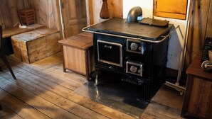 A rustic kitchen with a stove, wooden cabinets, and a wooden floor. - The Real Faroese Experience (Skalavik)