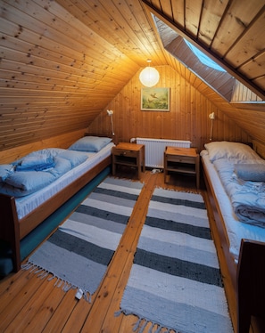 A cozy attic bedroom with two wooden beds, a small table, and a radiator. - The Real Faroese Experience (Skalavik)