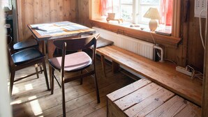 A wooden cabin interior with a dining table, chairs, a bench, a window with curtains, and a radiator. - The Real Faroese Experience (Skalavik)