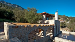 Une construction en pierre, dotée d’arches et d’un toit en tuiles, entourée de verdure et s’élevant sur un paysage montagneux.