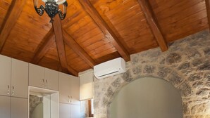 Une chambre avec un mur en pierre, des poutres en bois au plafond, un lit avec du linge de maison blanc, un luminaire suspendu et une cheminée en pierre.
