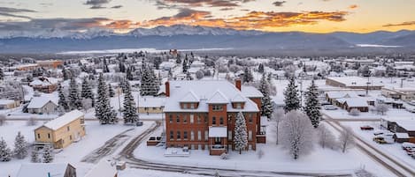 Un barrio residencial cubierto de nieve, con un edificio de ladrillo rojo destacado en el centro, rodeado de casas y árboles.