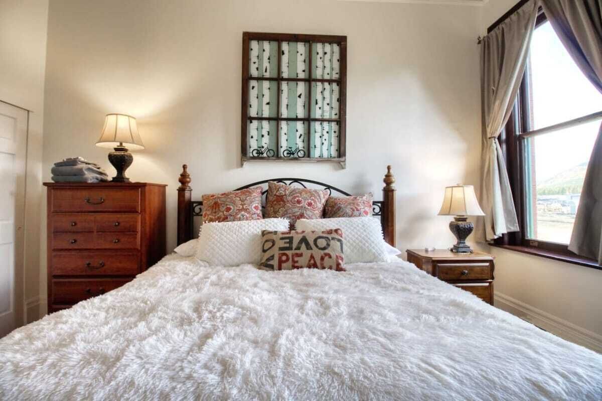 A bedroom with a bed, a dresser, a nightstand, a lamp, a window with curtains, and a wall-mounted picture.