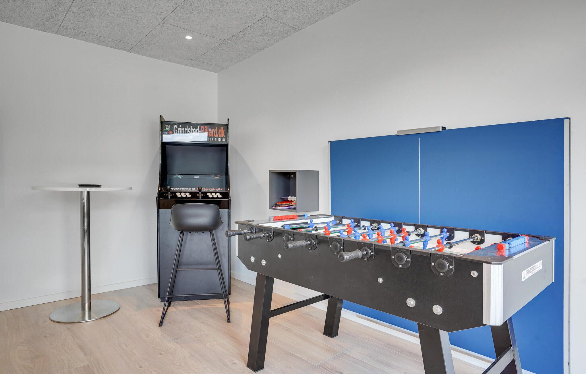 A room with a foosball table, a small bookshelf, and a chair.