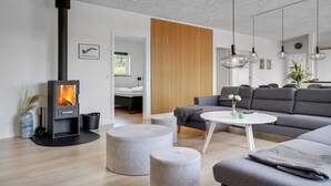 Ein modernes Wohnzimmer mit Kaminofen, grauen Sofas, Poufs und Pendelleuchten.