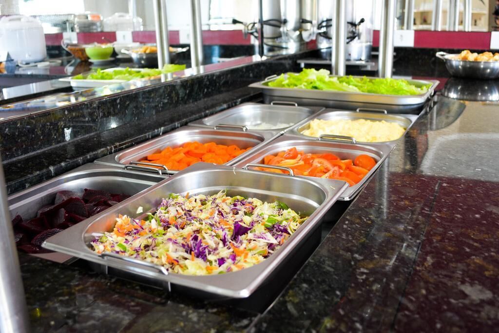 Un bufé con diversas opciones de comida, incluyendo ensalada de col, zanahorias y otras verduras mixtas.
