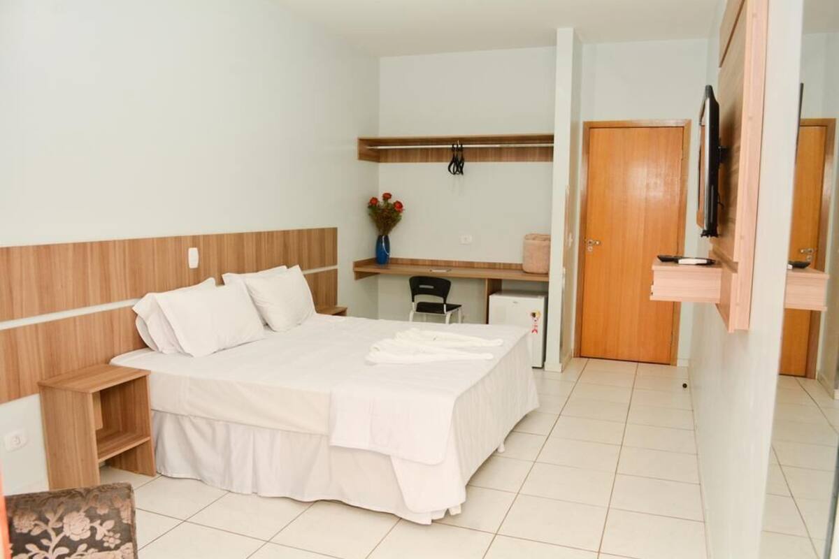 A hotel room with a bed, a desk, a chair, a TV, and a door.