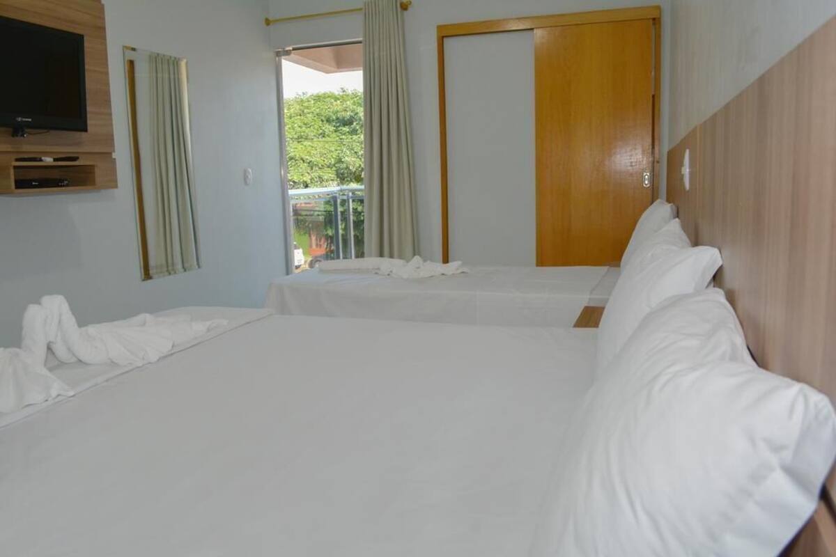 A hotel room with two beds, a TV, and a balcony with curtains.