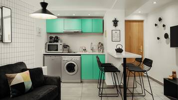 A compact kitchen with a washing machine, a microwave, and a sink. There is a dining area with two stools and a table.