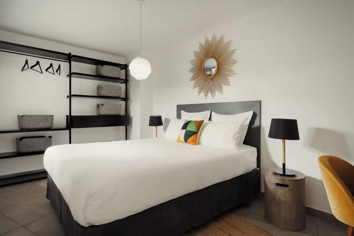 Une chambre à coucher moderne avec un lit, des lampes de chevet, un miroir et une étagère.