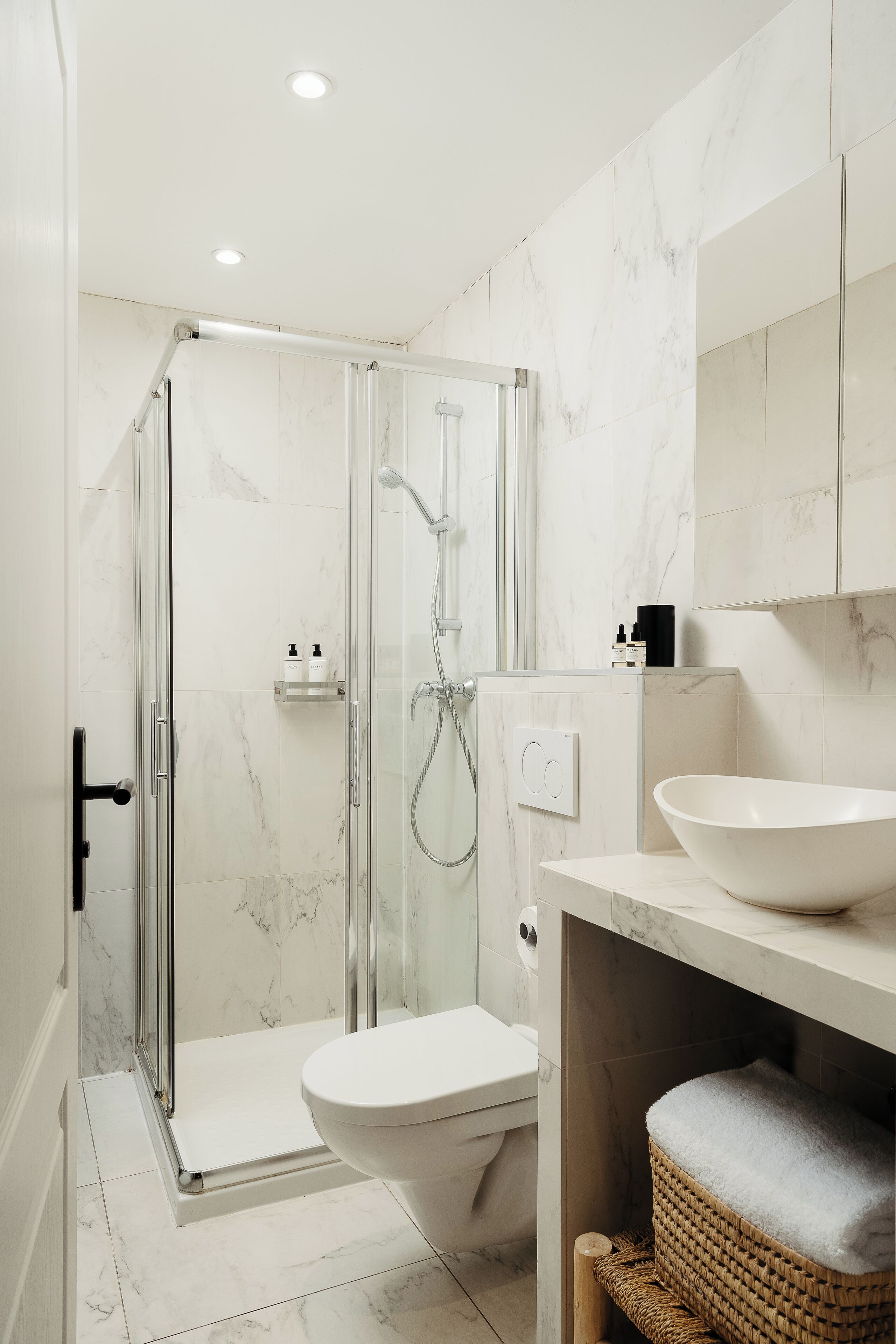 Et moderne badeværelse med en brusekabine med glasd ør, en hvid vask og et toilet.