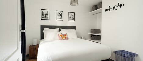 Un dormitorio ordenado con una cama grande, una lámpara colgante y tres cuadros en la pared.