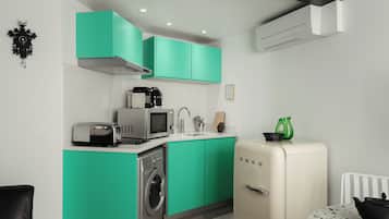 A compact kitchen with teal cabinets, a washing machine, a microwave, a toaster, and a vintage-style refrigerator.