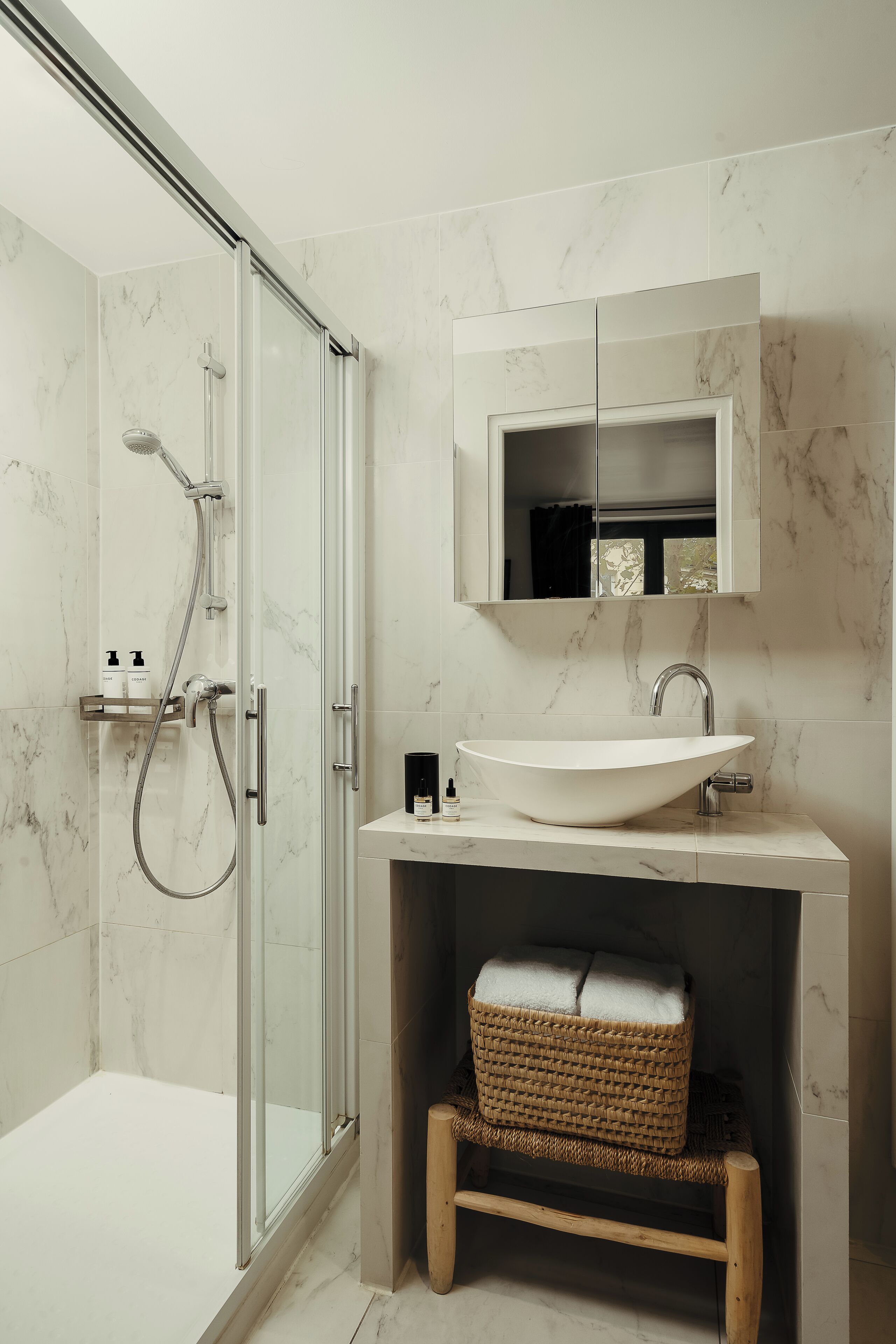 A modern bathroom with a glass-enclosed shower, a white sink, and a wooden bench.
