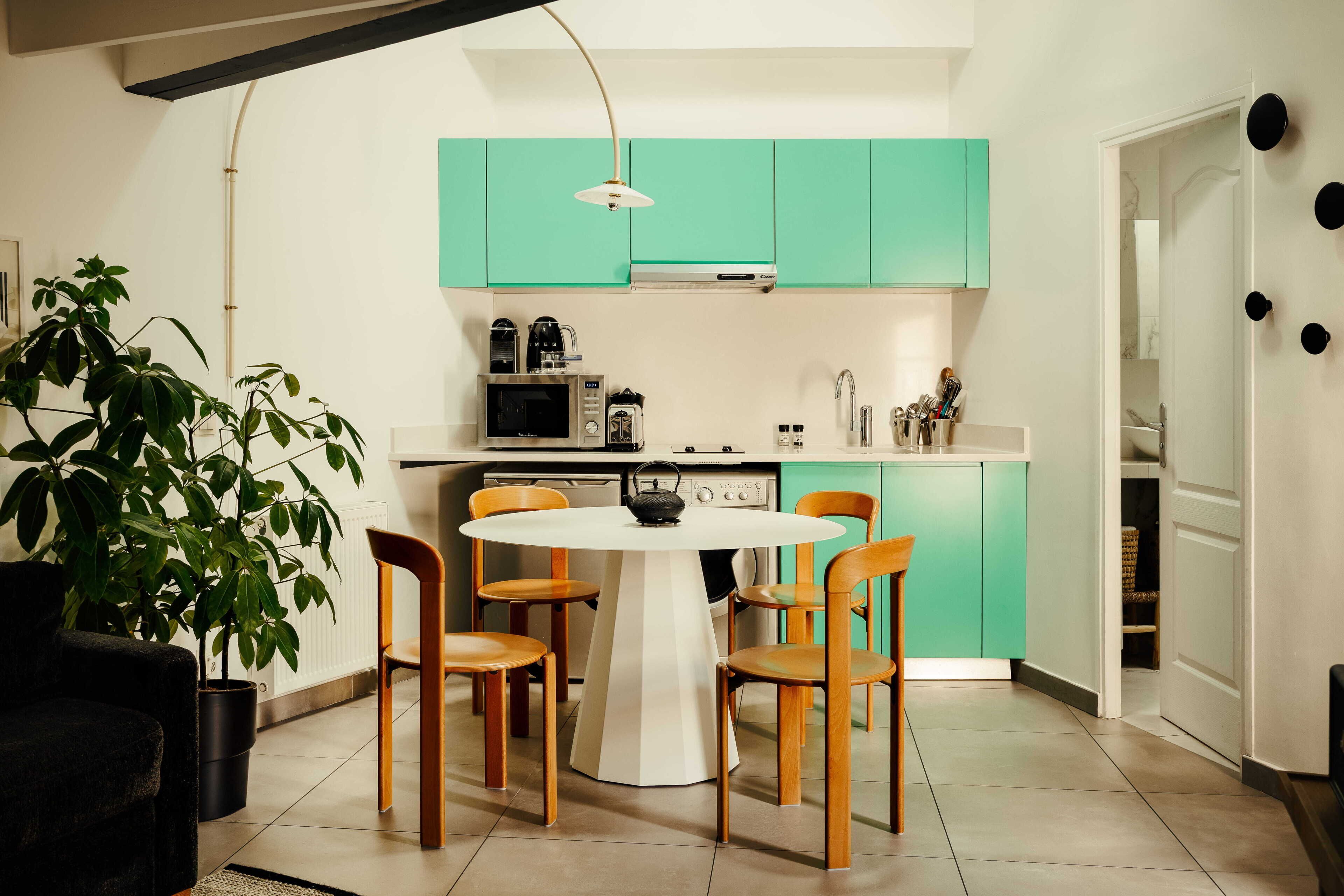 Una cocina moderna con armarios color turquesa, una mesa de comedor blanca y sillas de madera.