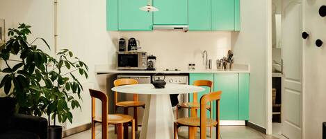 A modern kitchen with teal cabinets, a white dining table, and wooden chairs.
