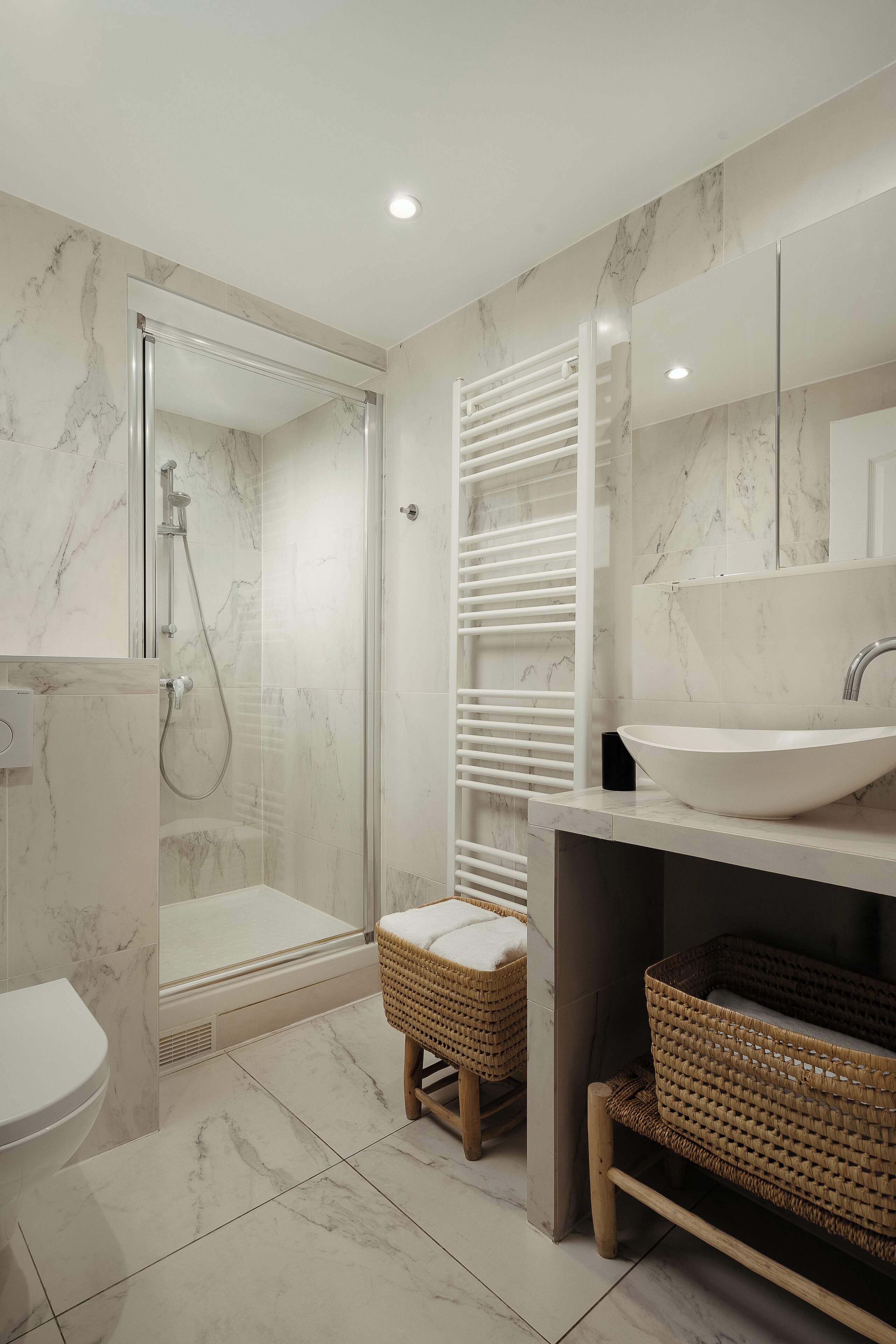 A modern bathroom with a glass-enclosed shower, a white sink, and marble flooring.