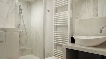 A modern bathroom with a glass-enclosed shower, a white sink, and marble flooring.