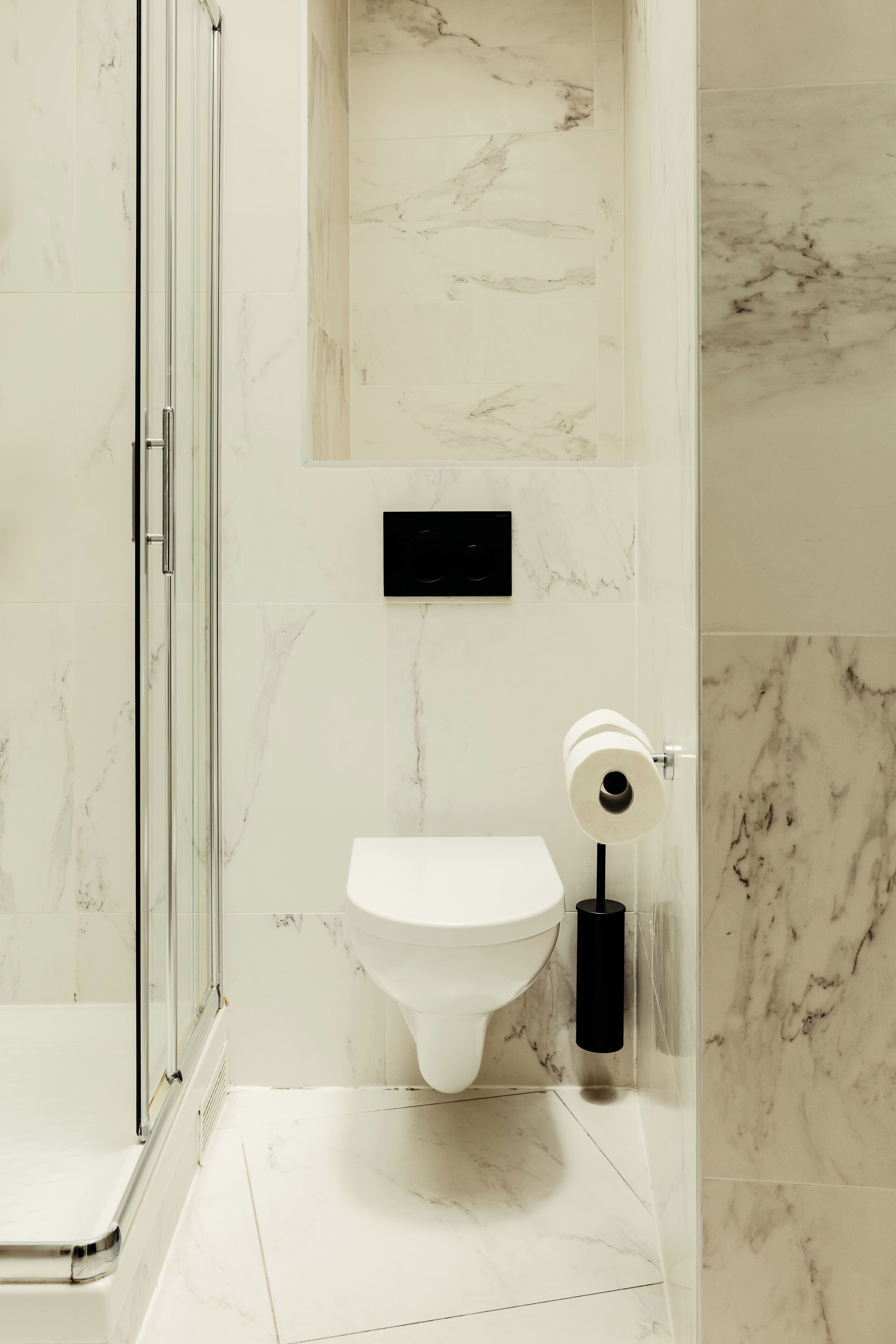 A bathroom with a toilet, a glass shower enclosure, and a marble floor.