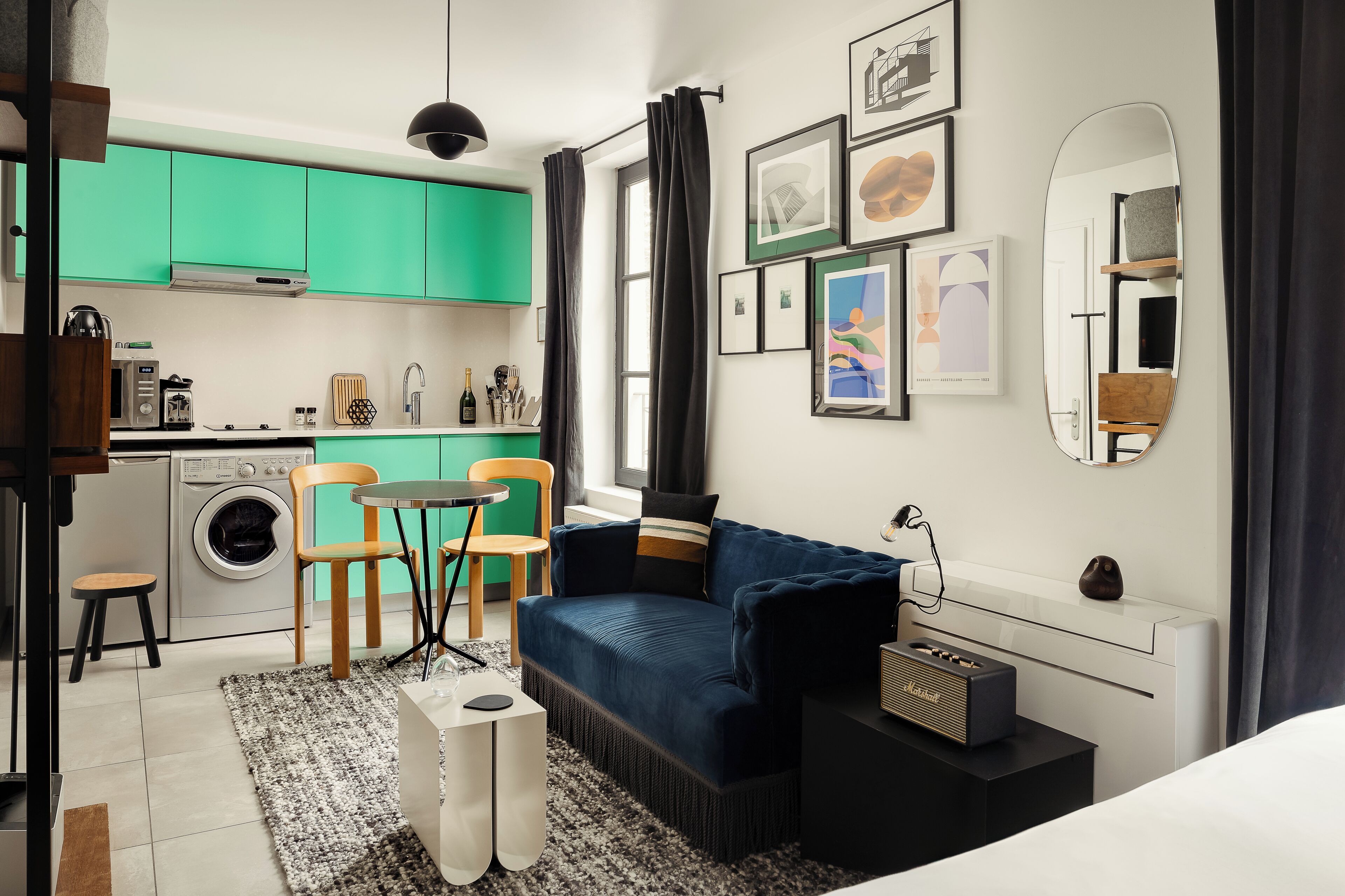 A compact living space with a kitchenette, a blue sofa, a small dining table, and a washing machine.