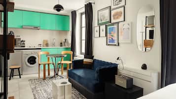 A compact living space with a kitchenette, a blue sofa, a small dining table, and a washing machine.