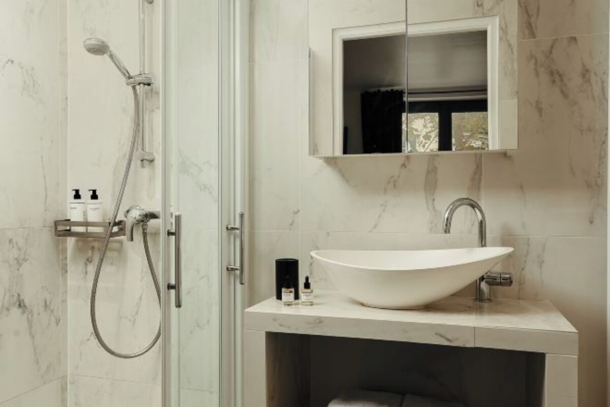 A bathroom with a large white sink, a mirror cabinet, and a shower with a handheld showerhead.