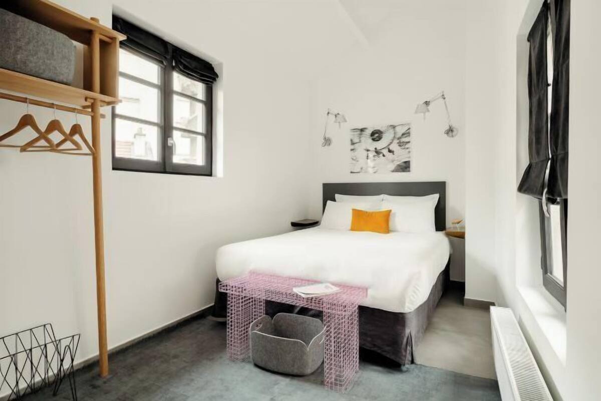 Une chambre à coucher comprenant un lit, un porte-manteau suspendu, une fenêtre, une œuvre d’art murale et une table de chevet.