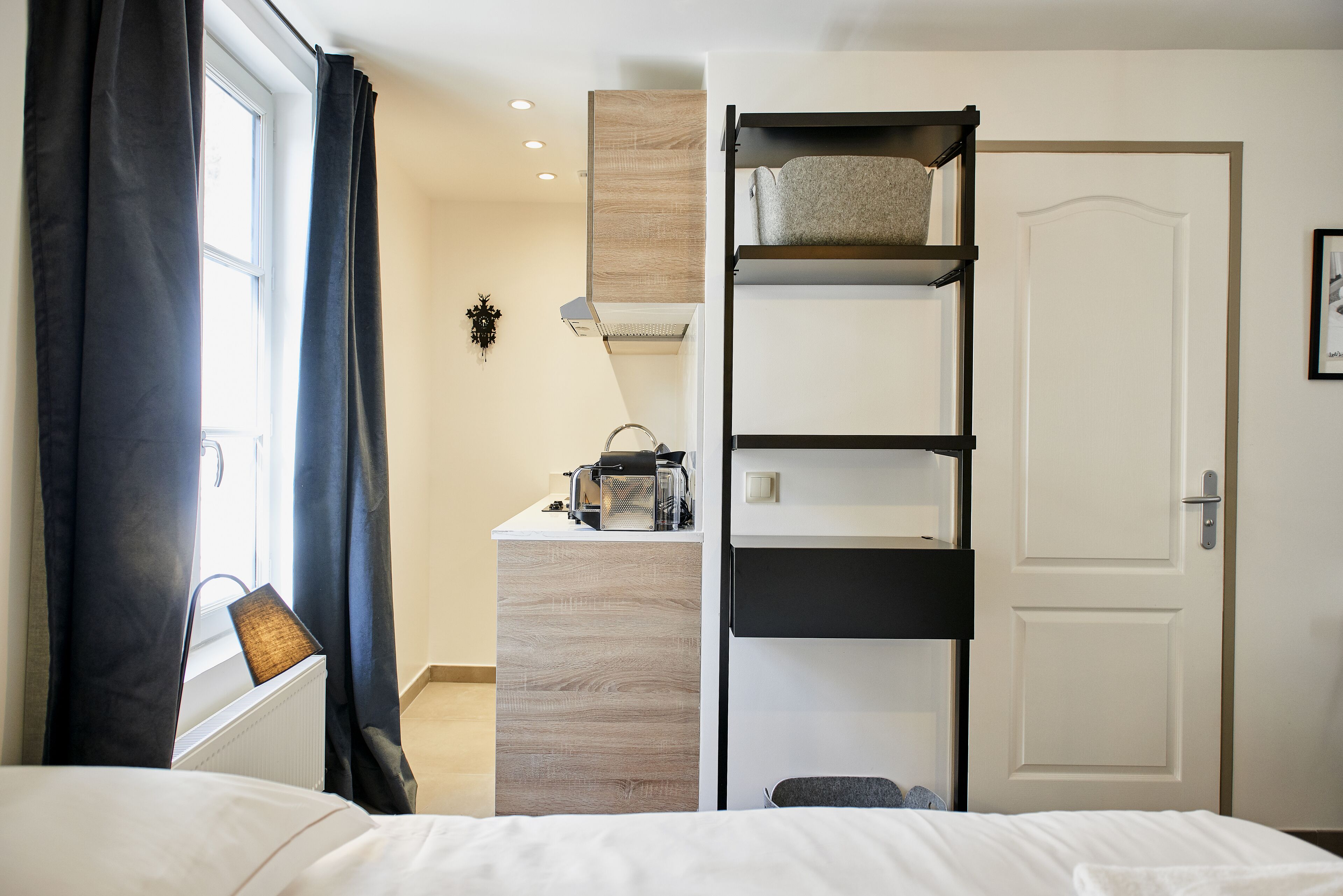 A bedroom with a bed, a desk with a computer, a radiator, a wardrobe, and a door.