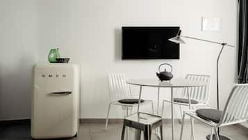 Habitació moderna amb nevera blanca, televisió de pantalla plana penjada a la paret, taula rodona de menjador amb cadires blanques i una làmpada de peu.
