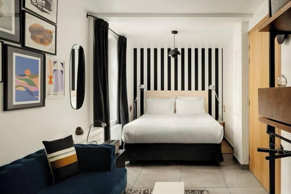 Une chambre d’hôtel moderne équipée d’un lit, d’un bureau, d’une chaise, d’un canapé et d’un mur orné de rayures verticales.