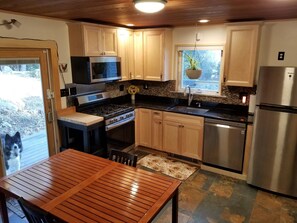 A modern kitchen with wooden cabinets, stainless steel appliances, and a dining area with a wooden table and chairs. - SUNAPEE RETREAT AT ENCHANTED FOREST - BRING KIDS - NEAR LAKE AND MOUNTAIN! (Newbury)