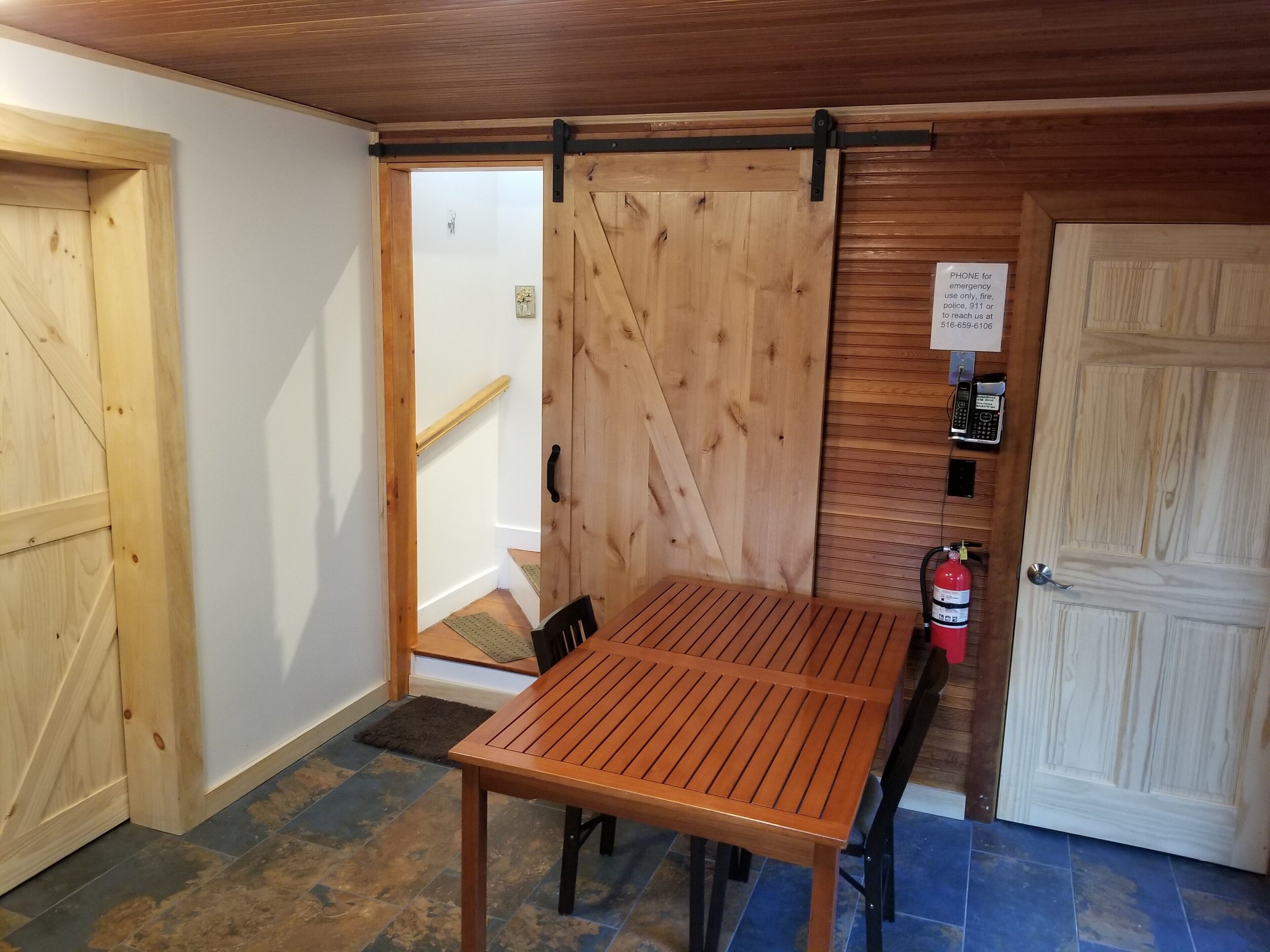 Een houten interieur met een tafel, stoelen, een brandblusser en een telefoon voor noodgevallen.