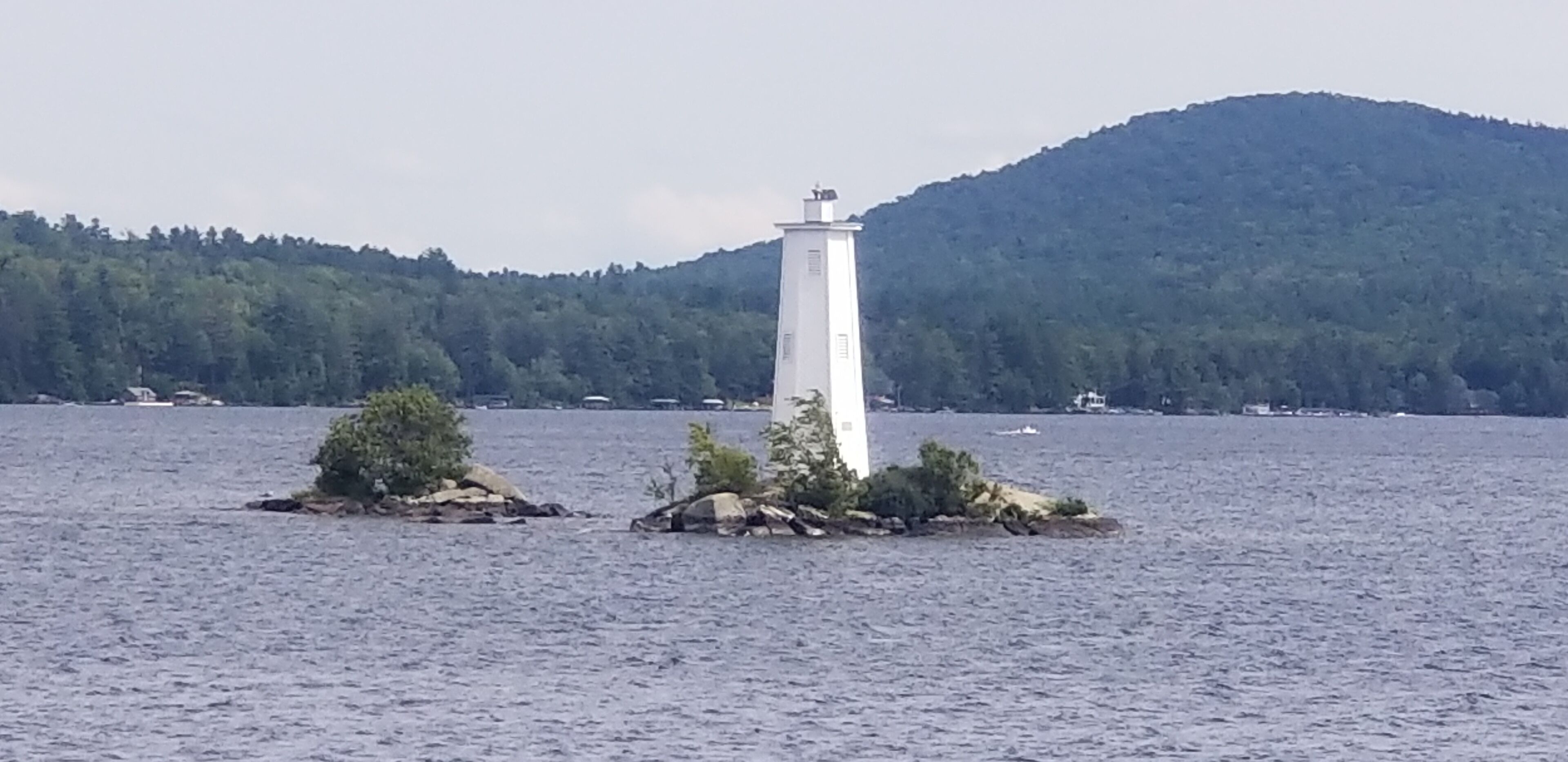 A lighthouse on a small island with a forested hill in the background.