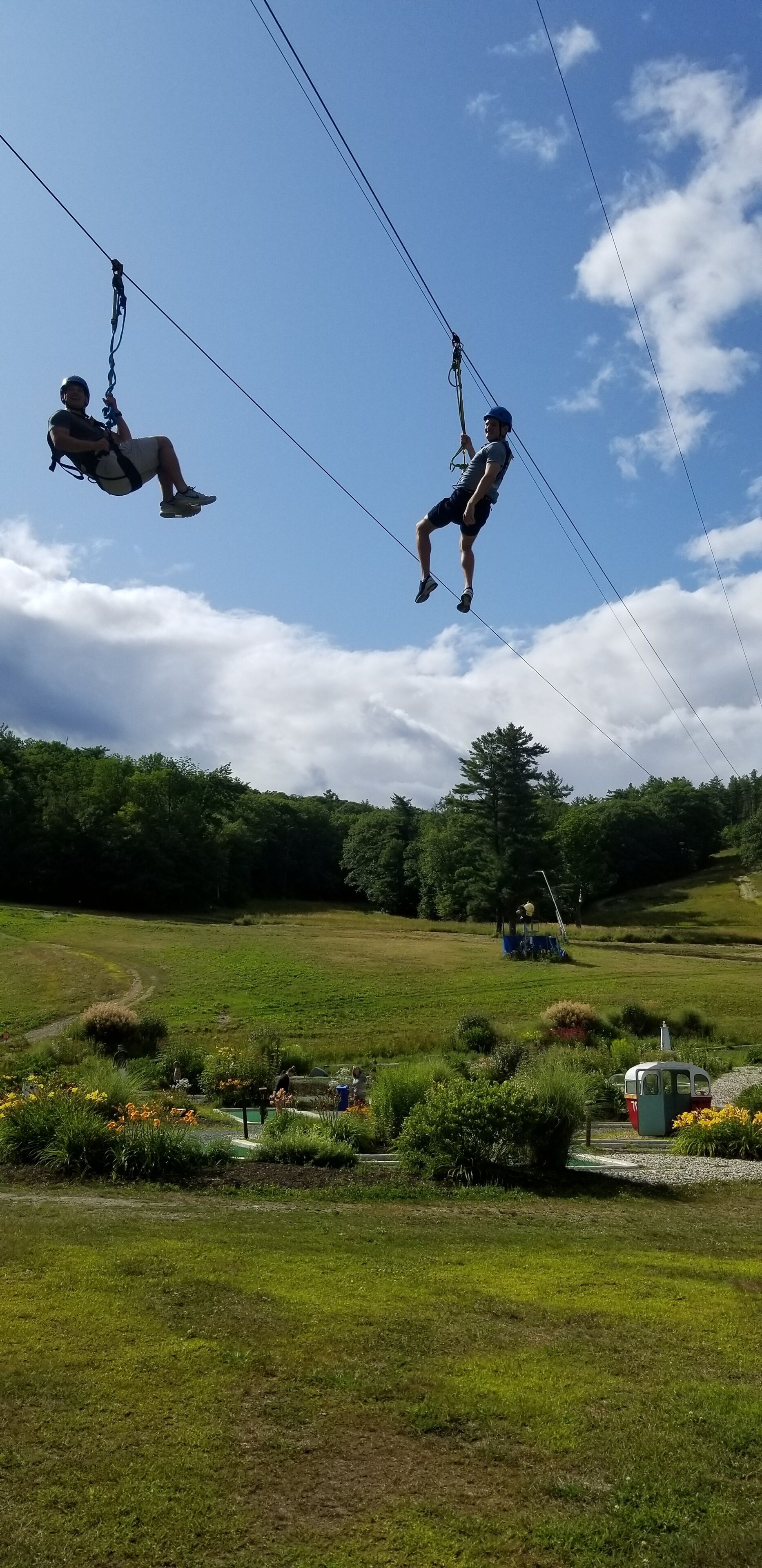 Eine Person saust mit einer Zipline über ein grasbewachsenes Feld, im Hintergrund sind Bäume zu sehen.