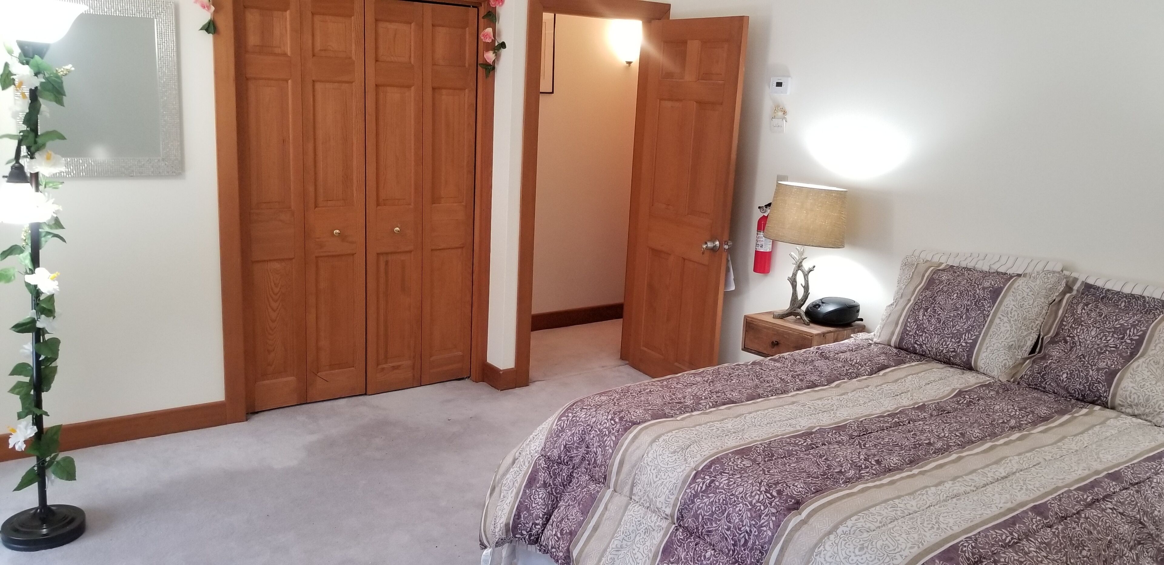 A bedroom with a bed, wooden wardrobe, and a nightstand with a lamp.