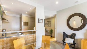 A modern kitchen with stainless steel appliances, a glass dining table with chairs, and a round mirror on the wall. - Waterfront Beauty with Parking by Zodiak Stays (Auckland)