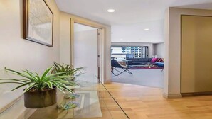 A modern interior with a glass table, potted plants, and a view into a living area with a sofa and chairs. - Waterfront Beauty with Parking by Zodiak Stays (Auckland)